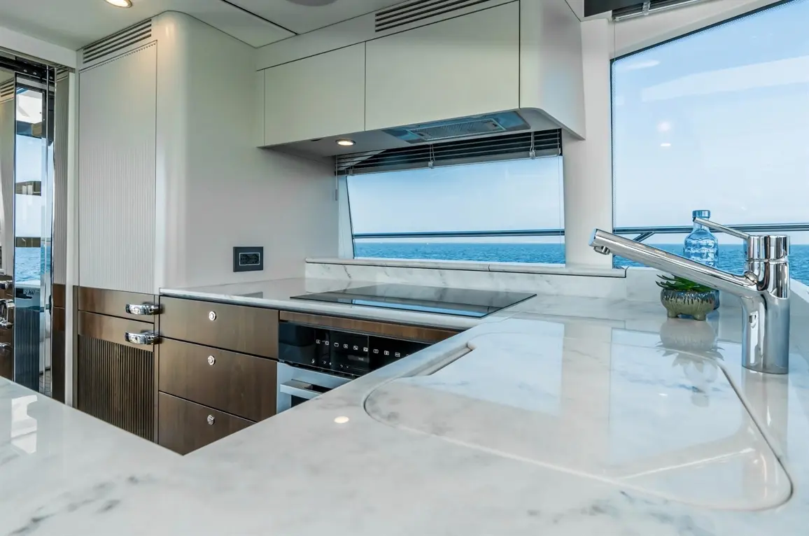 Modern yacht kitchen featuring sleek cabinetry, marble countertops, a view of the ocean, and a chrome tap with a water bottle.
